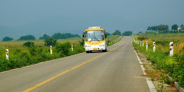 ein Reisebus fährt auf einer Straße mit grünen Wiesen links und rechts