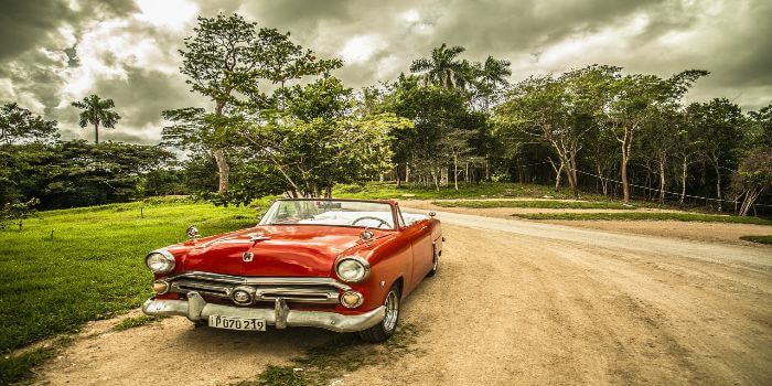 ein Oldtimer Cabrio steht am Straßenrand und dahinter ein Wald