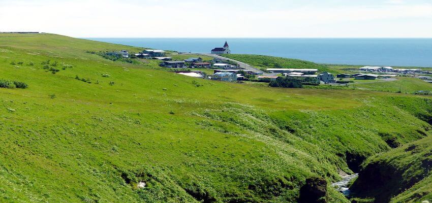 Kleines Dorf umgeben von grünen Wiesen und im Hintergrund das Meer.