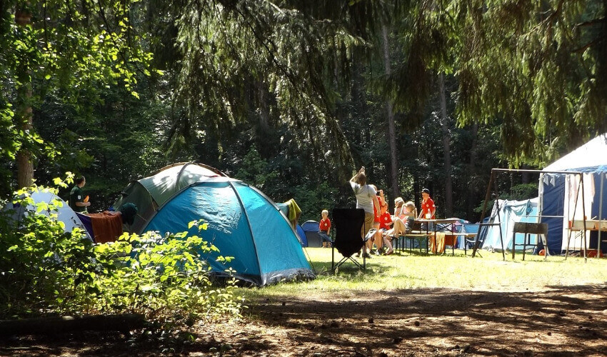 Familien sitzen auf einer Klappgarnitur zwischen Zelten.