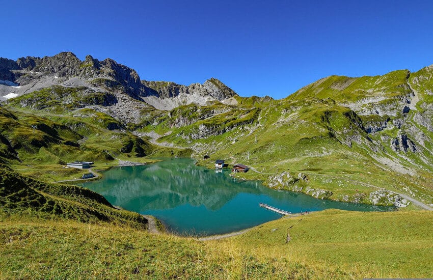 Ein kleiner See, umgeben von mit Gras bewachsenen Bergen.