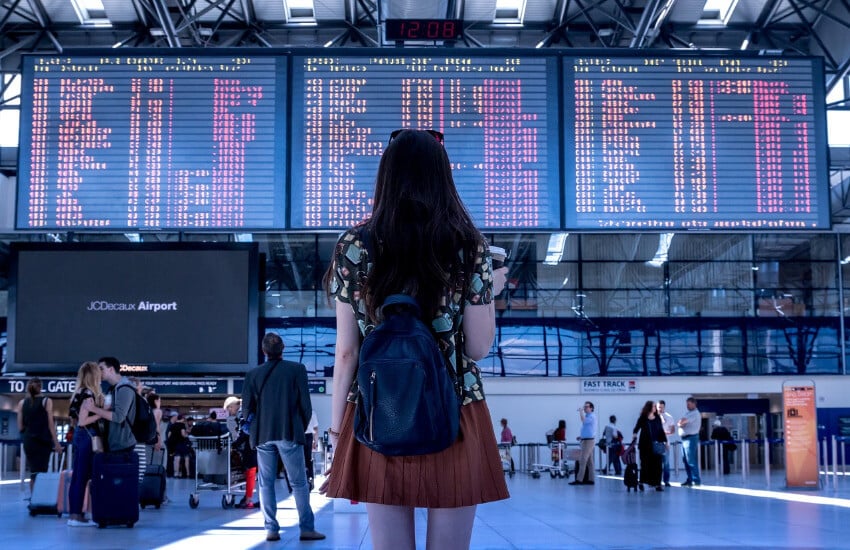Eine Frau blickt Richtung drei großer Anzeigetafeln am Flughafenterminal.