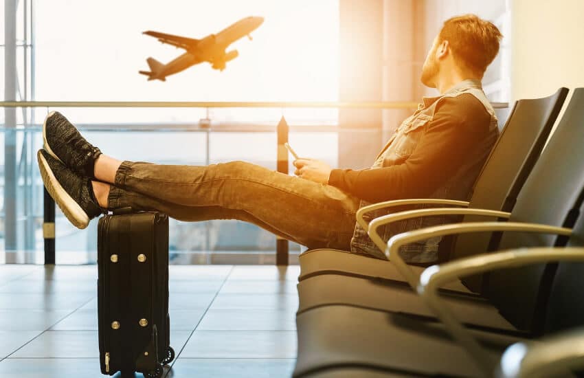 Ein Mann sitzt im Wartebereich eines Flughafenterminals und beobachtet ein Flugzeug beim Start.