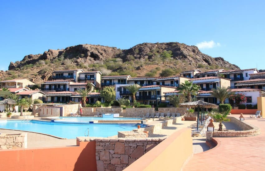 Ein Bild von einem Resort auf den Kapverden mit Pools und Liegebereich. Im Hintergrund einzelne Hotelgebäude und Bungalows.